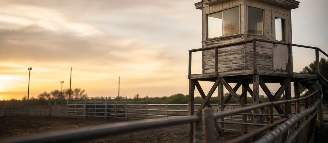 A raised timber announcer box above an empty rodeo arena in evening light