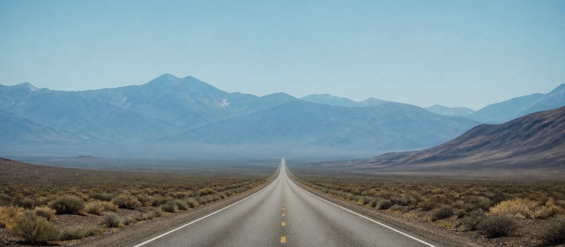 An empty two-lane highway running across sagebrush basin toward distant mountains