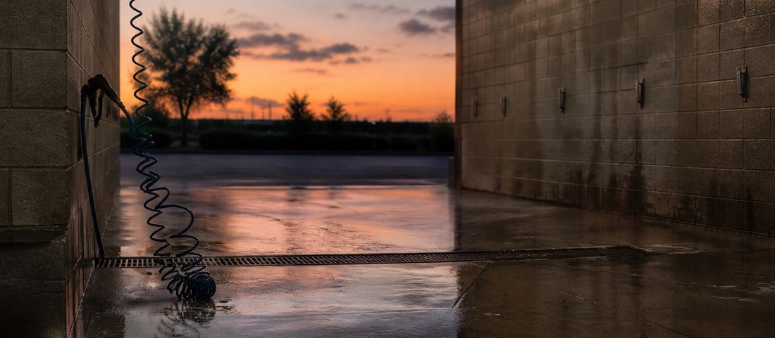 A self-service car wash bay at dusk with wet concrete and a coiled hose