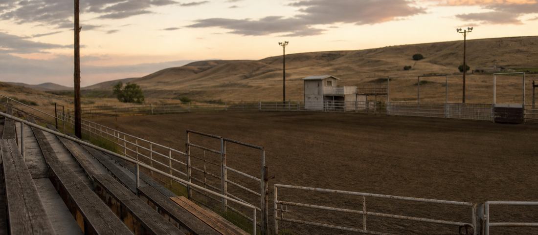An empty county rodeo arena with wooden bleachers and pipe panels at dusk